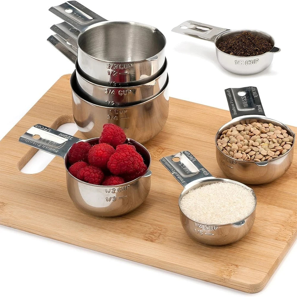 A stainless steel measuring cup and spoon set with various sizes and a wooden cutting board.