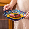 Una mano sostiene un plato de ensalada y pasta de cerámica azul y naranja lleno de salsa amarilla y carne en una prenda de co