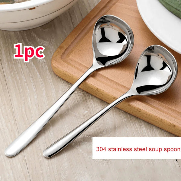 A pair of shiny stainless steel soup spoons resting on a wooden cutting board.