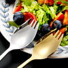 A set of two stainless steel cutlery pieces, a fork and a spoon, resting on a plate with a salad.
