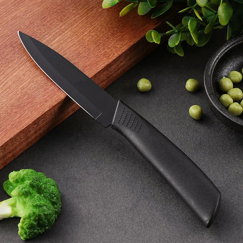 A black utility knife with a silver blade rests on a dark surface next to broccoli florets and green olives.