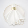 A stack of white cotton table napkins tied with a gold ring band, displayed on a light beige plate.