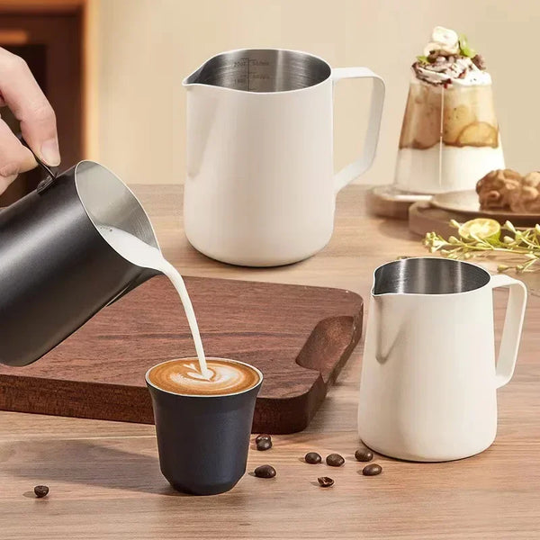 Ein schwariger Edelstahl-Kaffeepfifferschlucker gießt Milch in eine kleine Tasse auf einer Holzoberfläche.