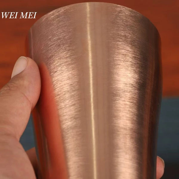 A hand is holding a handcrafted vintage copper coffee mug with a smooth, rose gold finish.