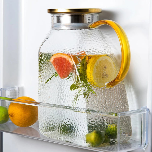A large glass water jug filled with water and citrus fruits, including lemons and oranges, sitting on a shelf.