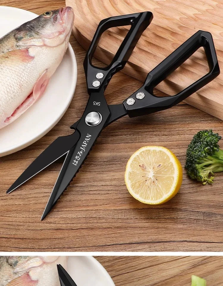 A pair of black titanium kitchen shears with silver accents rests on a wooden surface next to a fish and a lemon slice.