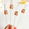 A hand holds a set of reusable glass straws with small teddy bear charms.