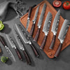 A set of professional Damascus chef knives displayed on a wooden cutting board with surrounding produce.