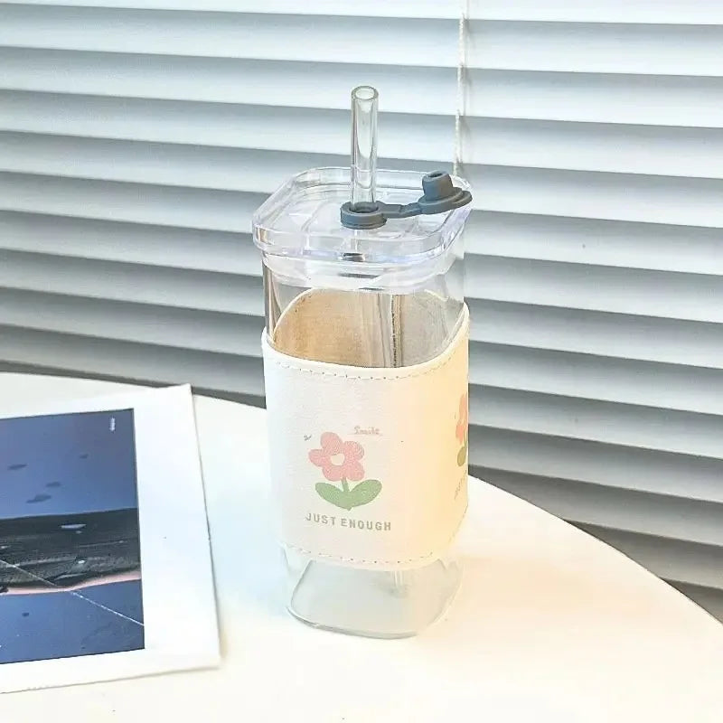 A clear glass drink cup with a lid and straw, featuring a light beige sleeve decorated with a pink flower.