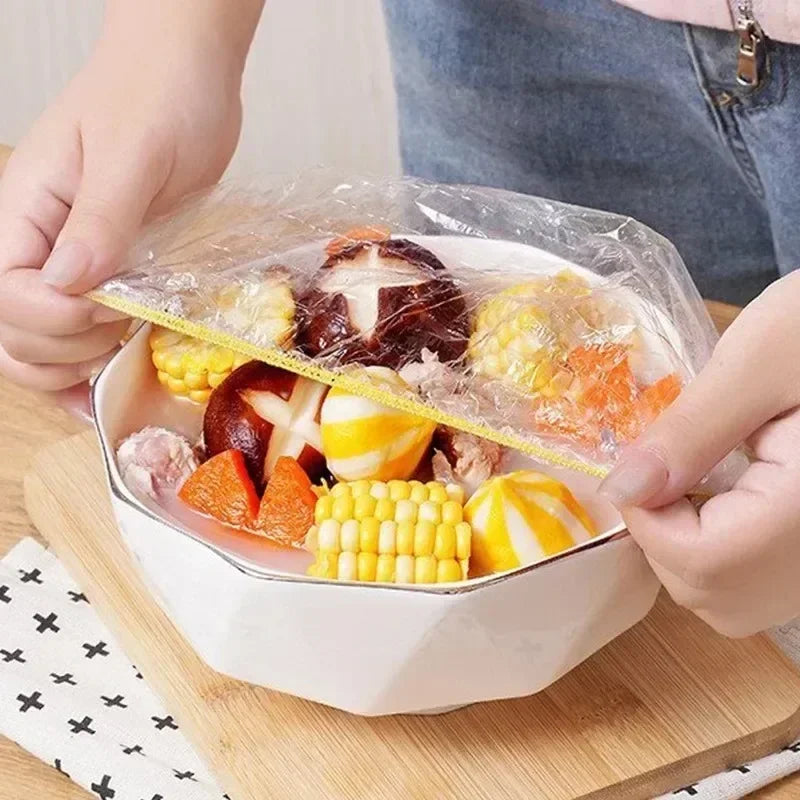 Hands are opening a clear reusable food storage bag filled with various fruits and vegetables on a wooden cutting board.