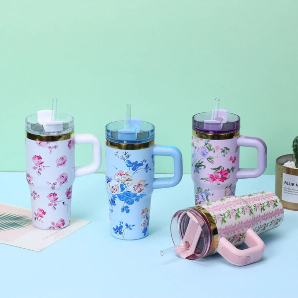 A pink and blue patterned stainless steel insulated travel tumbler with a clear lid is shown against a light green background