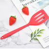 A bright red silicone flat bottom frying spatula is shown next to a fresh strawberry on a white marble surface.
