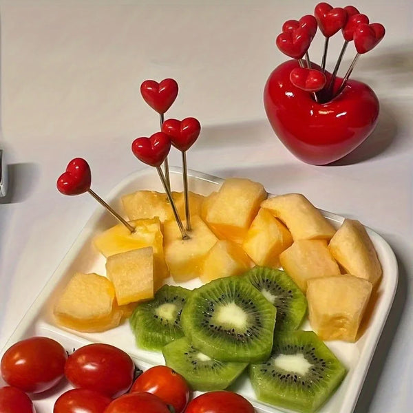A white dish holds sliced fruit pieces and a red apple with heart-shaped decorations.