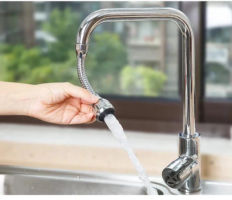 A hand is operating a chrome kitchen faucet with a flexible hose, spraying water into a sink.