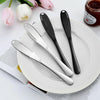 A set of three stainless steel butter knives resting on a white plate next to a jar of jam.
