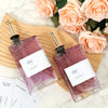 A glass oil and vinegar dispenser set with labels and funnel resting on a wooden board surrounded by pink roses.