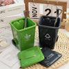 A green novelty trash can and matching green food scoop are displayed on a woven mat.
