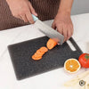 A hand is using a knife to slice carrots on a black marble texture cutting board.