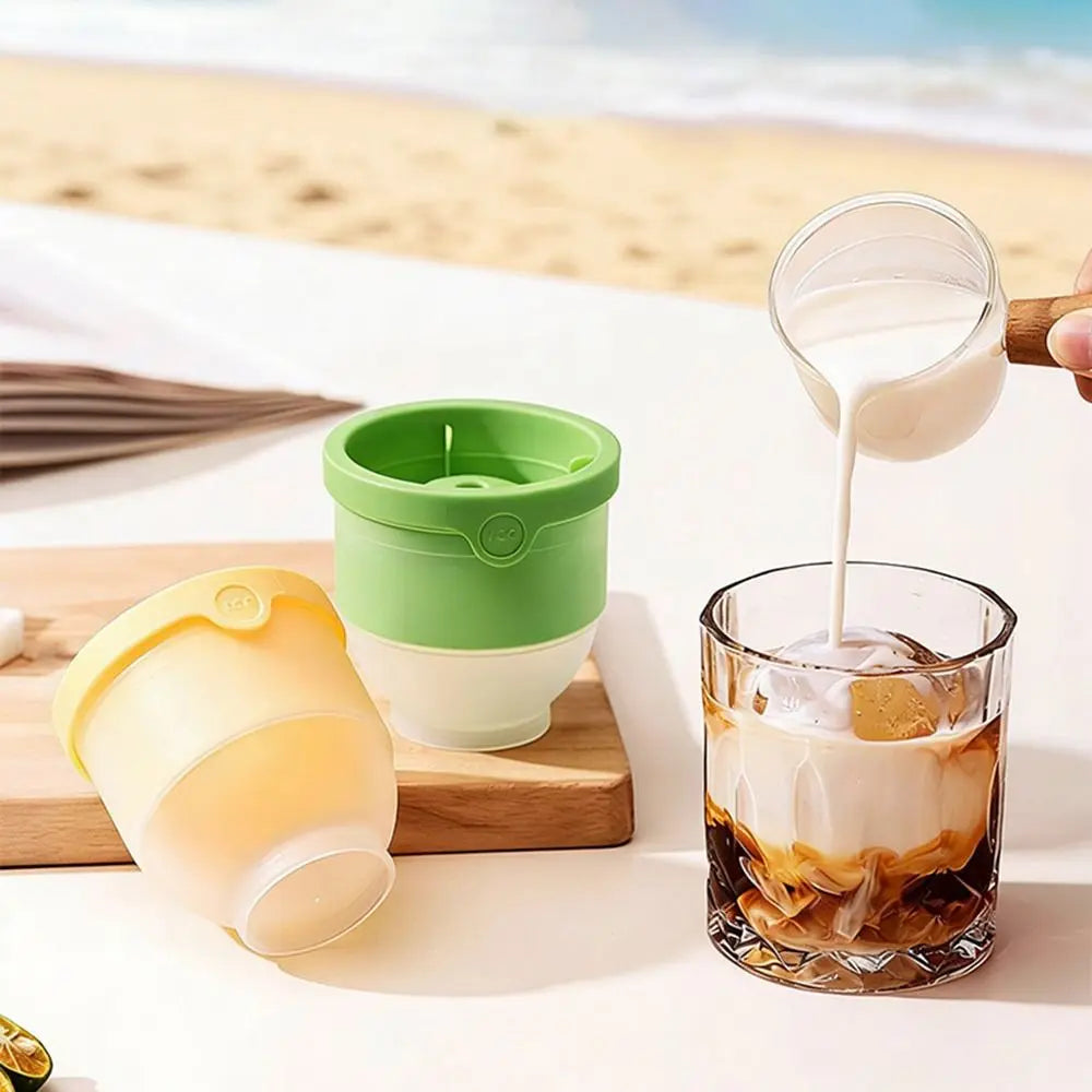 Set de moldes reutilizables de bolas de hielo de silicona con un recipiente verde y una taza amarilla junto a una copa de caf