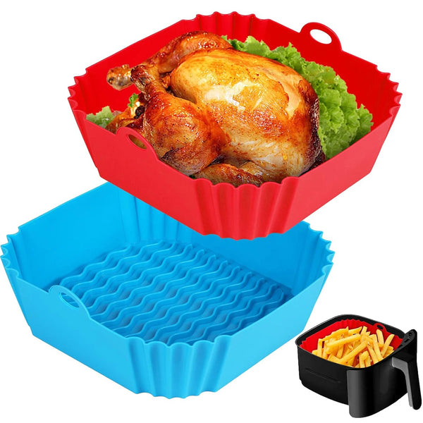 Roter Silikon-Airfryer-Einsatztopf gefüllt mit gegrilltem Hähnchen und grünen Gemüse, neben einer blauen Silikon-Backform.