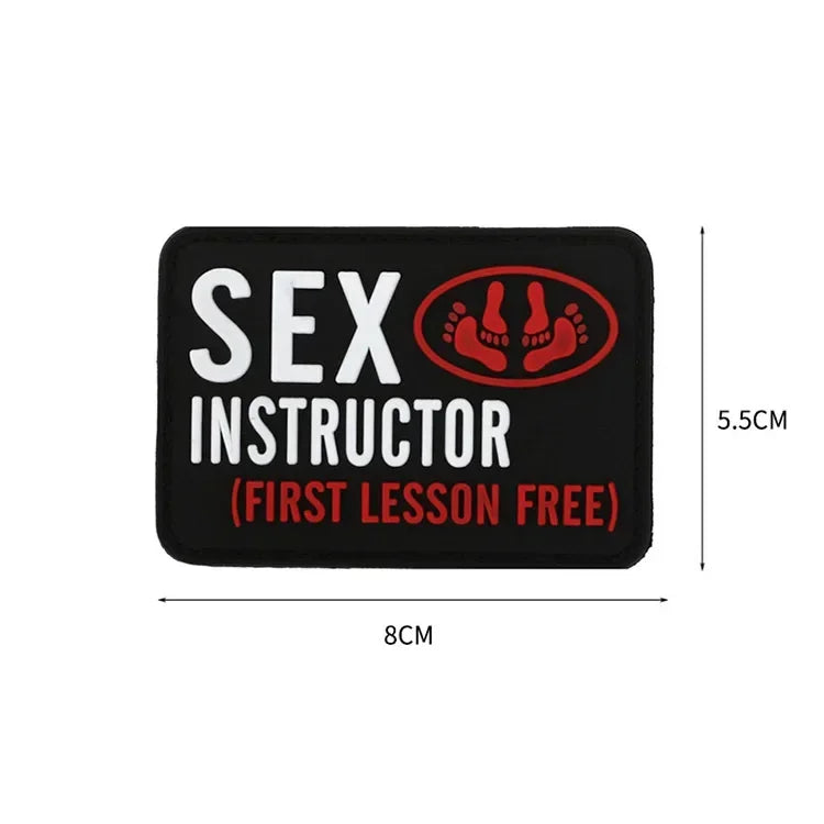 Black rectangular patch with white text SEX INSTRUCTOR (FIRST LESSON FREE) and a red icon of feet.