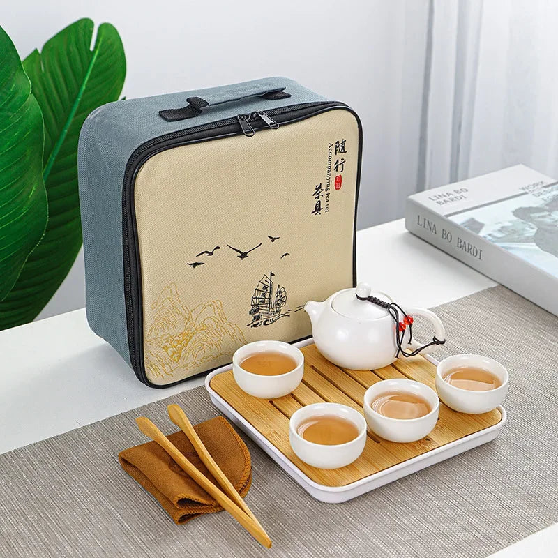 A light blue zippered pouch containing an elegant ceramic tea set with cups and a teapot on a wooden tray.