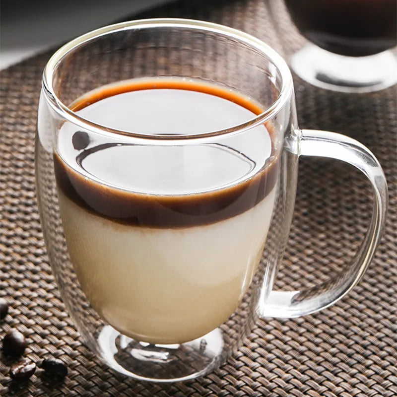Klares doppelwandiges Borosilikatglas-Kaffeebecher mit geschichtem Kaffee, dunkle Flüssigkeit auf heller Schicht