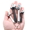A hand holds a set of two small metal adjustable spanner wrenches with attached chains.