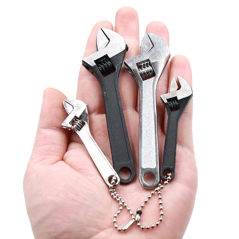A hand holds a set of two small metal adjustable spanner wrenches with attached chains.