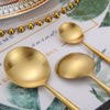 A set of matte gold stainless steel spoons and a beaded necklace displayed on a white plate.