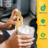 Hands are using a gold precision syrup pump dispenser to fill a white glass with liquid.