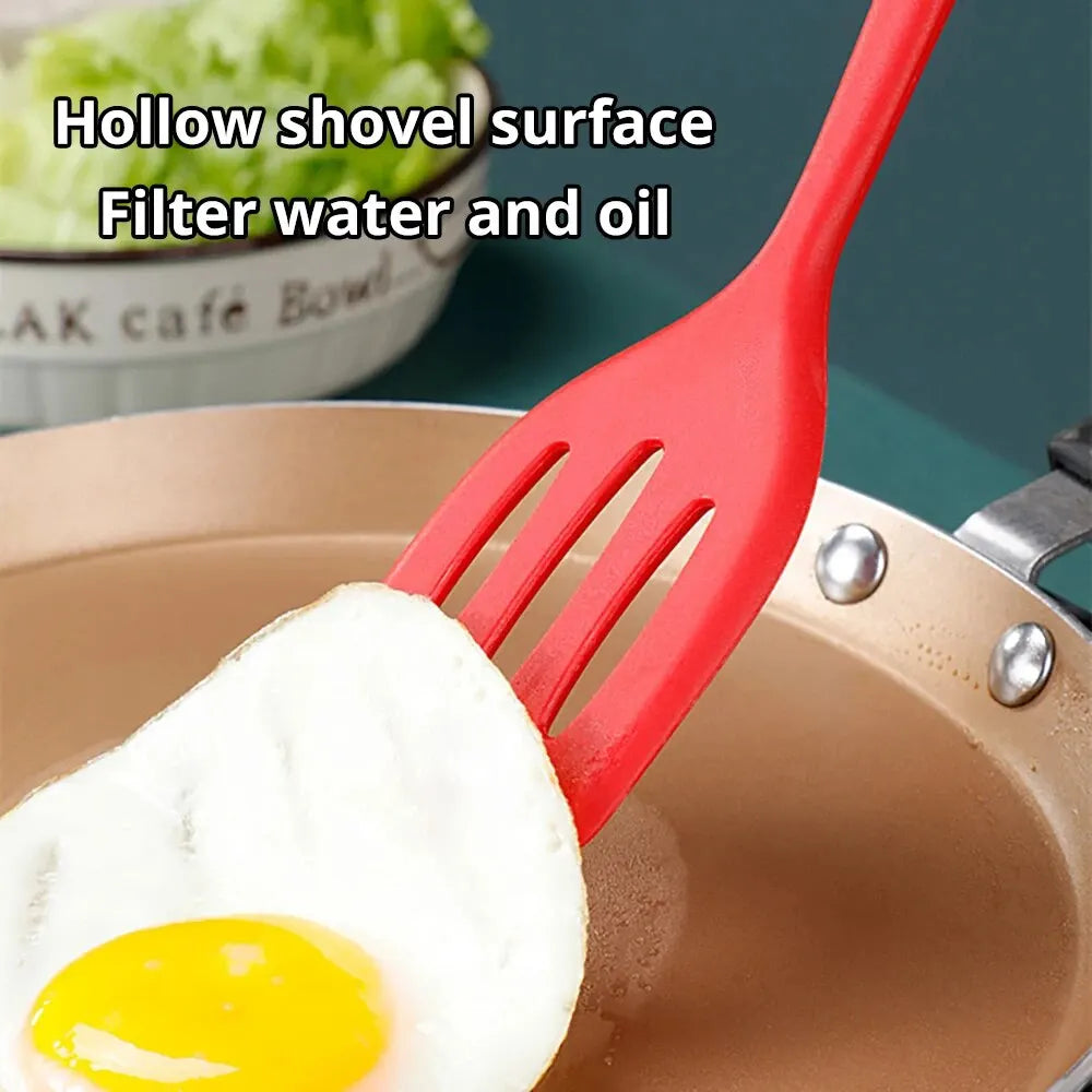 A red silicone flat bottom frying spatula is shown lifting a fried egg from a cooking pan.