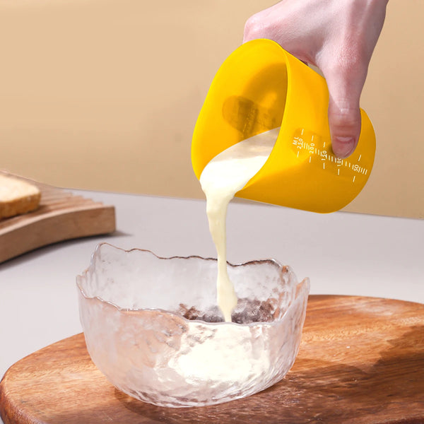 Eine Hand gießt eine weiße Flüssigkeit aus einer gelben flexiblen Silikonmessbecher in eine Glasschale.