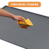 A hand is cleaning a dark gray silicone under sink drain tray with a yellow sponge.
