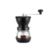 Molinillo de café manual de cerámica negra con tolva de vidrio y mecanismo de molienda metálico.