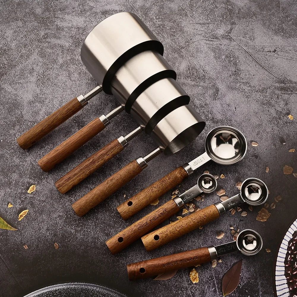 A stainless steel measuring set with wooden handles is displayed on a dark surface.