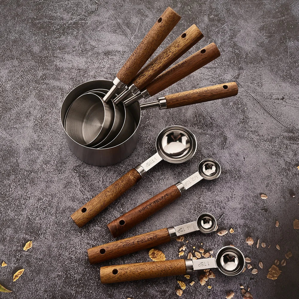 A set of four wooden-handled stainless steel measuring spoons arranged on a gray surface.