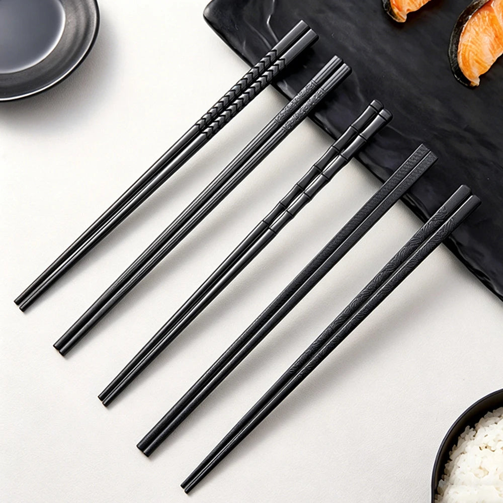 A set of five pairs of black reusable anti-slip plastic chopsticks laid diagonally on a dark slate board.