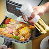 A hand is spraying oil from a white bottle into a cooking appliance filled with fried food.