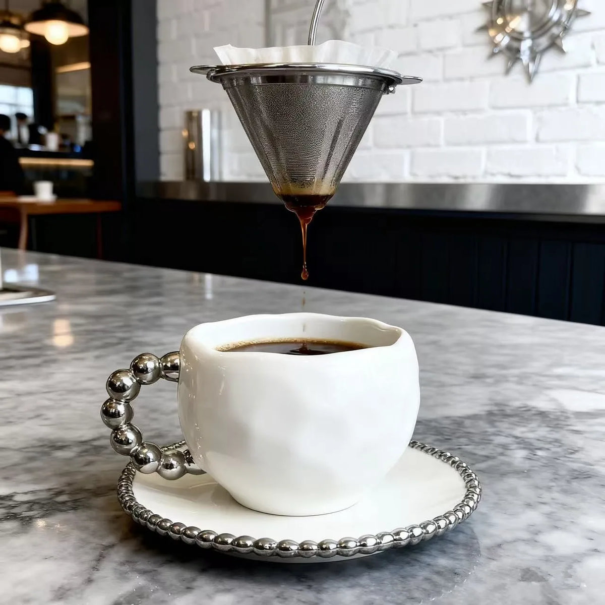 Un filet de café foncé est versé dans une théière en céramique blanche et son dessous de plat sur une table en marbre.