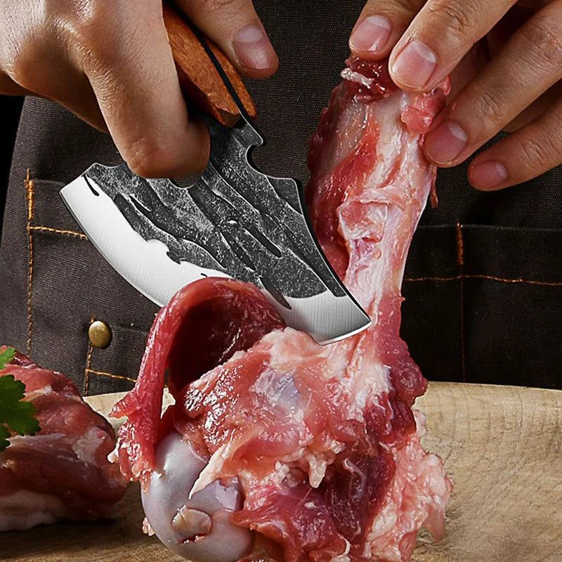 Hands are using a forged stainless steel meat cleaver to cut raw meat on a wooden board.