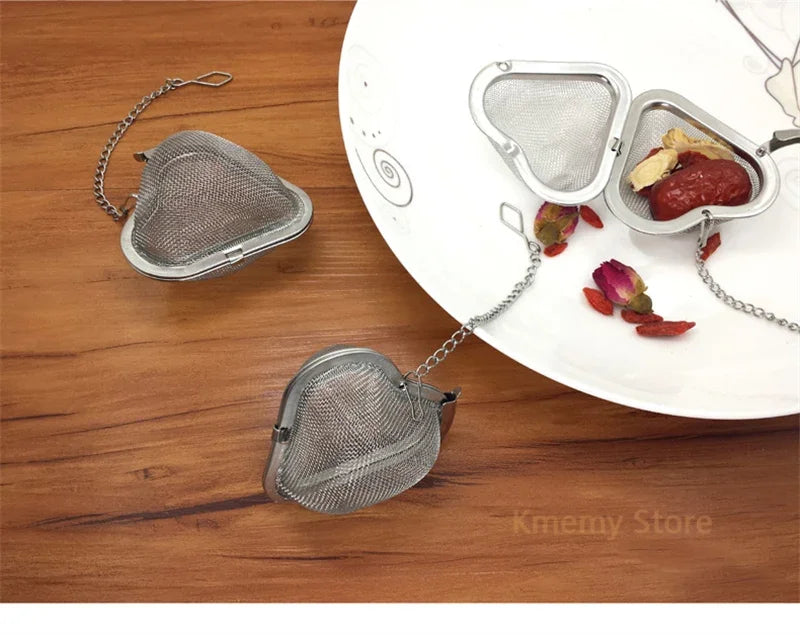 Stainless steel tea infuser ball with chain used to strain loose leaf tea, spices, and herbs on a white plate.
