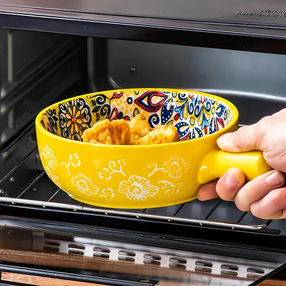 A hand is holding a yellow ceramic salad bowl with a handle, filled with golden-brown food, inside an oven.