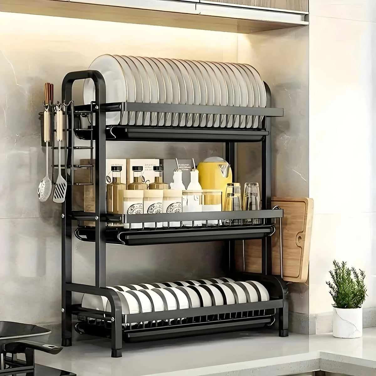A black 3-tier vertical kitchen utensil dish rack holding plates, cutlery, and various kitchen tools.
