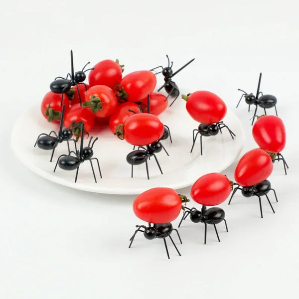 A set of reusable animal appetizer forks featuring black and red insects and fruit on a white plate.