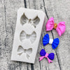 A silicone baking mold tray containing various pink, blue, and purple bow shapes for chocolate cupcakes.