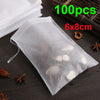 A clear plastic disposable tea filter bag with a drawstring is shown on a dark surface next to loose spices and tea leaves.