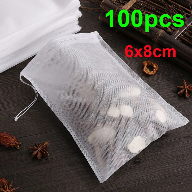 A clear plastic disposable tea filter bag with a drawstring is shown on a dark surface next to loose spices and tea leaves.