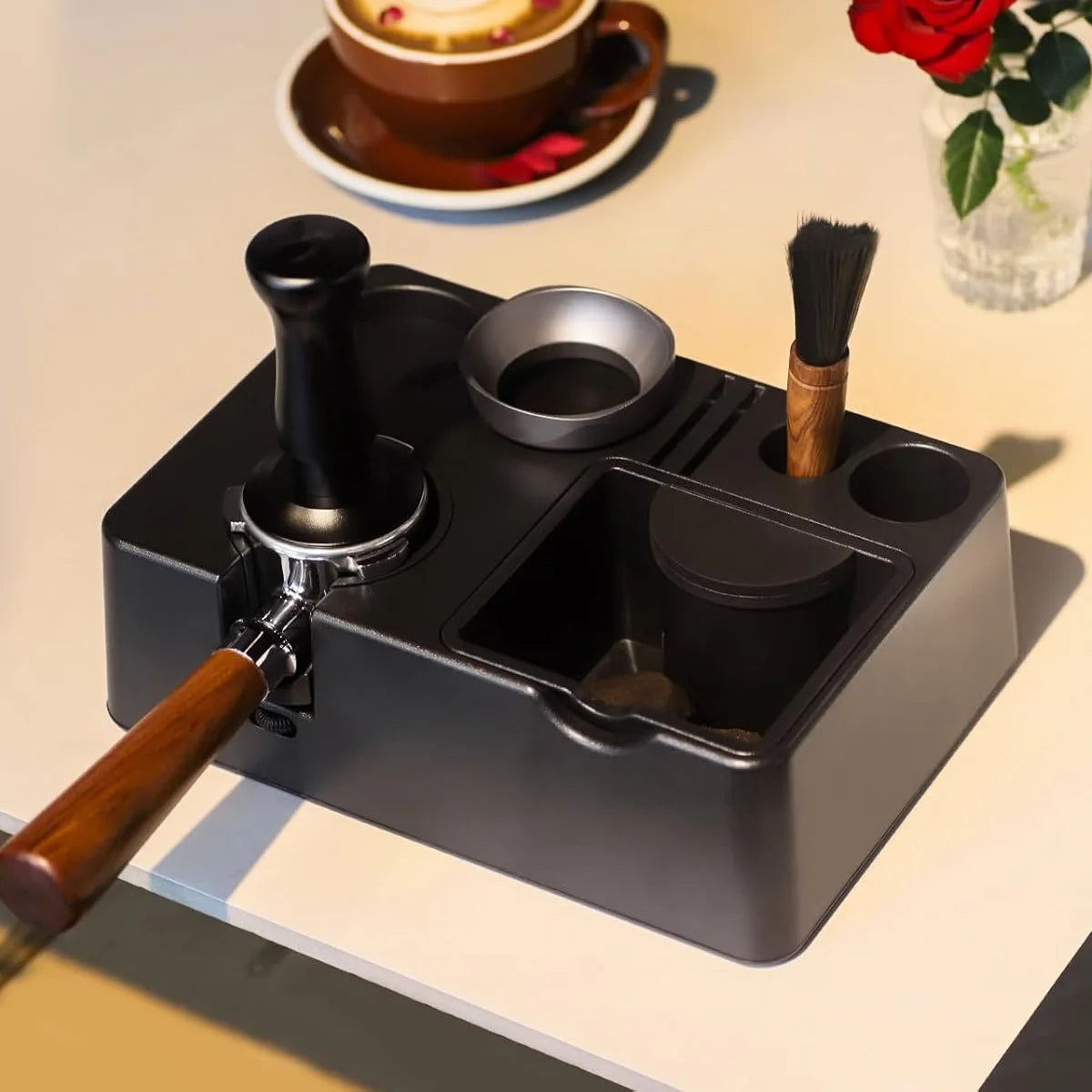 A black espresso tamping station organizer with a wooden handle and various tools is shown on a light surface.