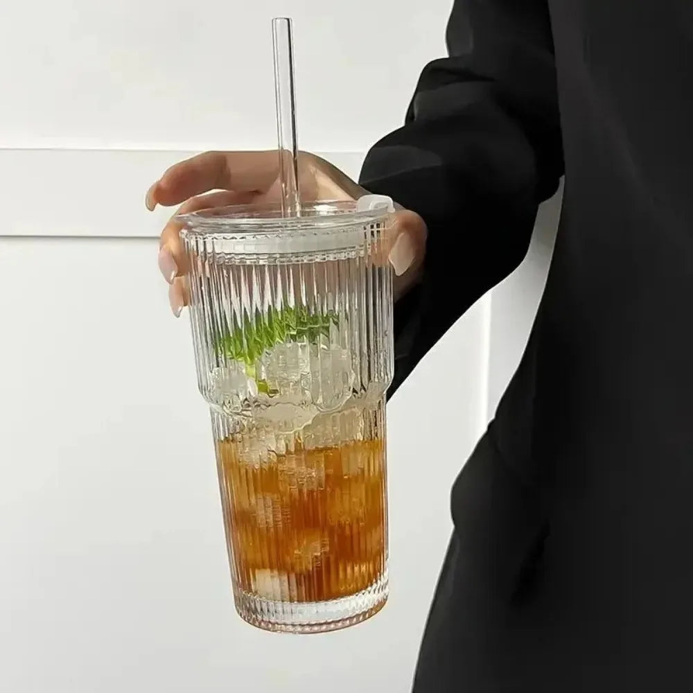 A hand holds a glass drinking cup filled with iced tea and mint, featuring a clear glass, lid, and straw.